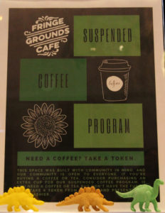 Photo of a poster with the words Suspended Coffee Program on it. Tiny plastic dinosaurs line the front of the poster.