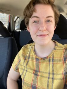 Selfie of a human smiling with brown hair, wearing a plaid yellow shirt.