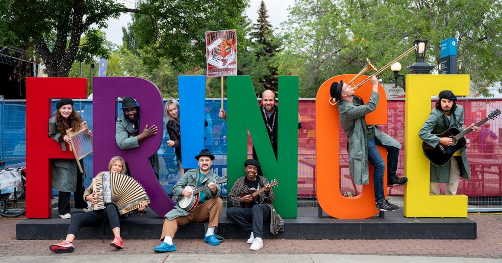 Artists with musical instruments pose around the Fringe sign.