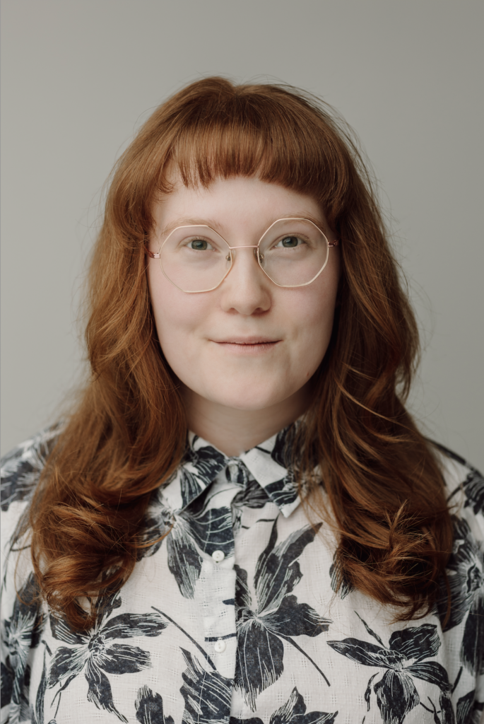 AJ Hrooshkin headshot. They have red hair and a button up shirt.