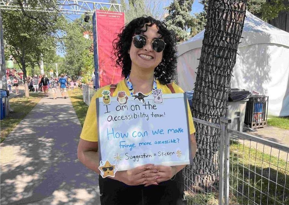 A Volunteer in sunglasses holding a small whiteboard Sayin "i am in the accessibility team.