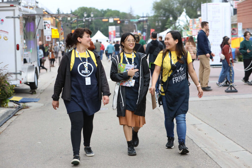 Three volunteers wearing aprons that say "ask me how to Fringe" on it, taking a stroll down the fringe grounds.