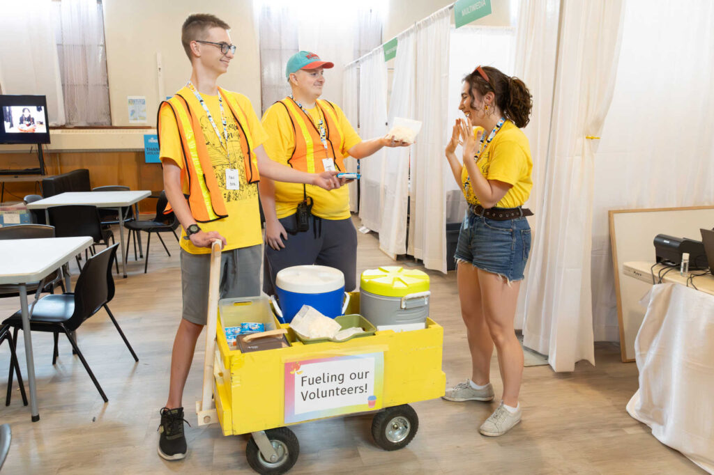 Two volunteer team members pulling a wagon full of goodies offering another volunteer a snack