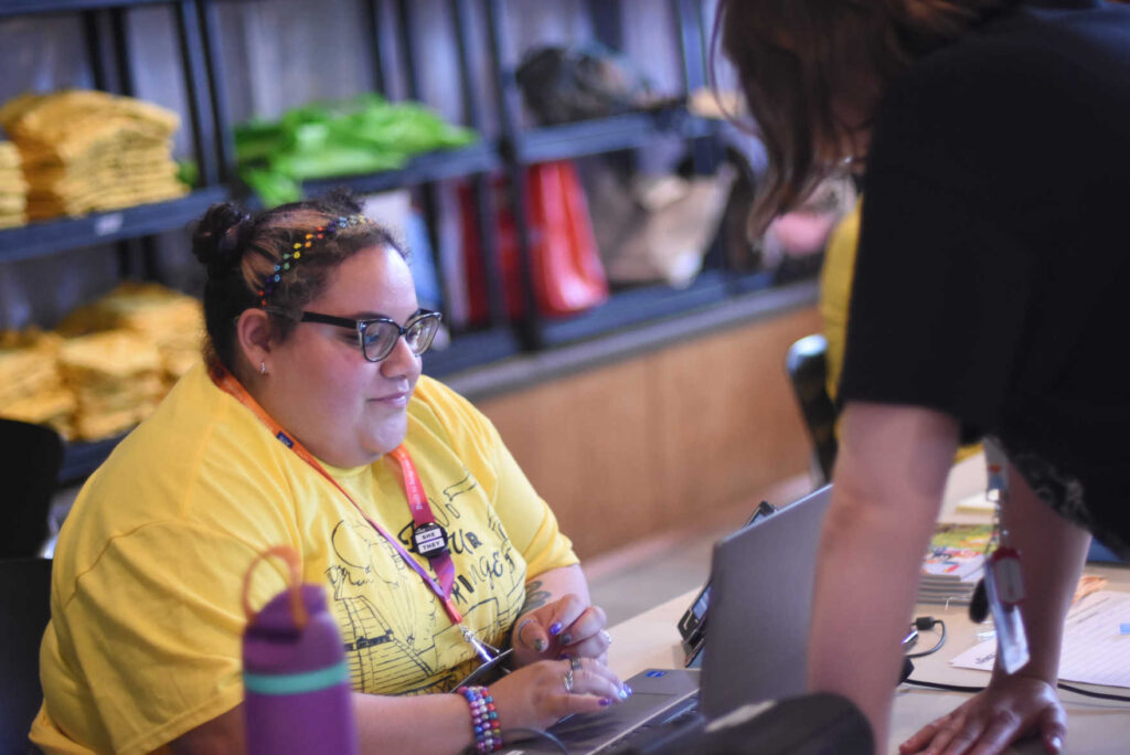 A Volunteer in a yellow shirt using a computer in Frings Theatre's Volunteer Headquarters.