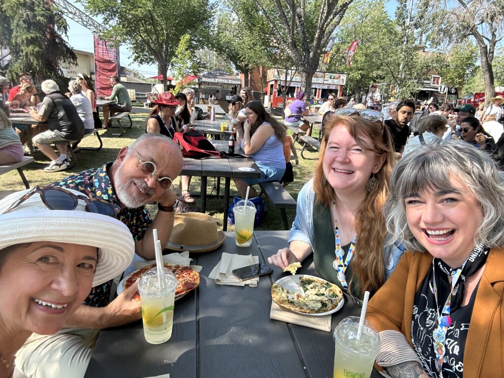 Four people sit around a table on Fringe grounds smiling.