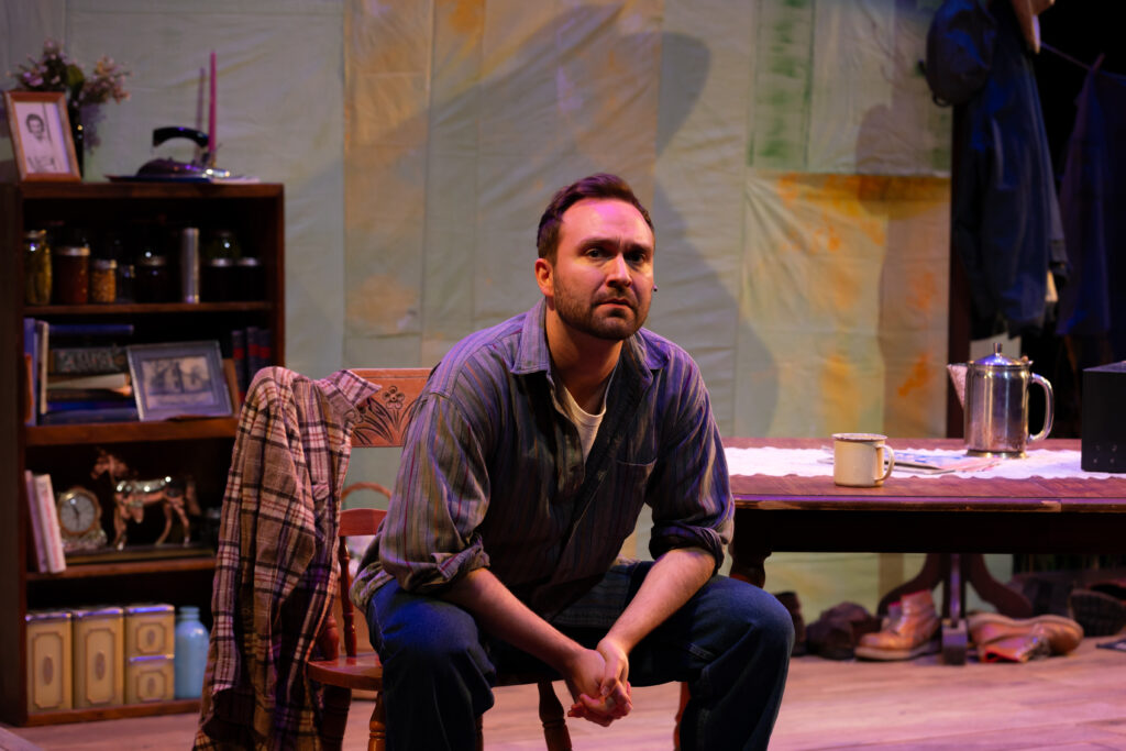 A man in a button up shirt sits and stares at the audience.