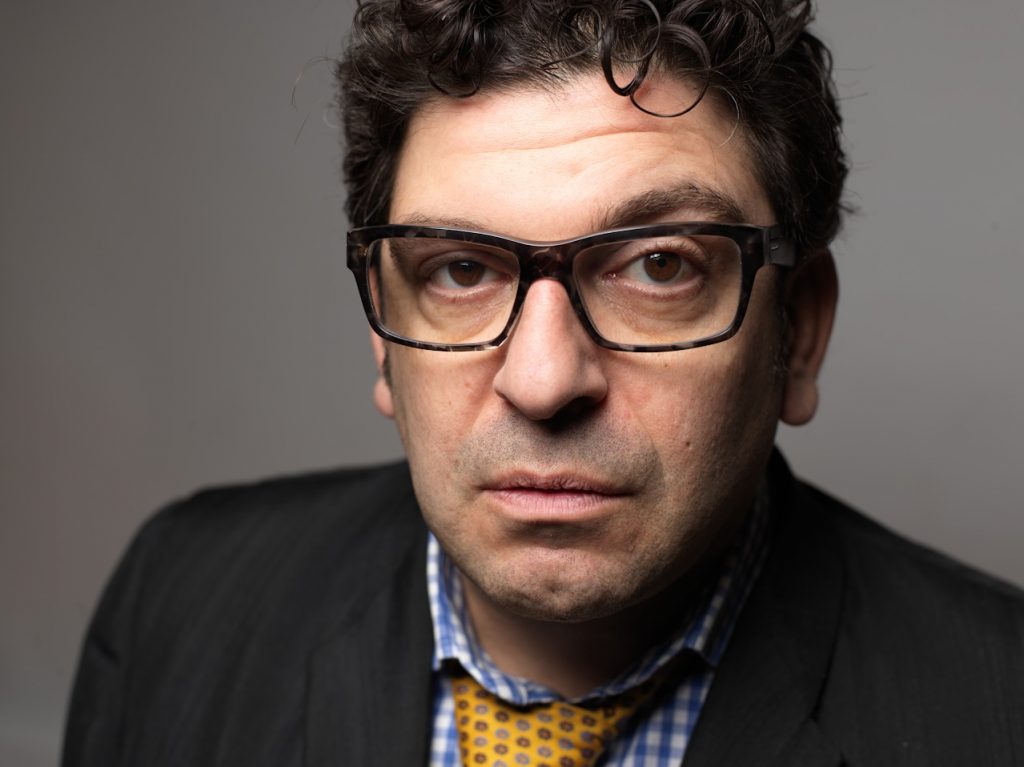 The artist is wearing a tie and glasses.