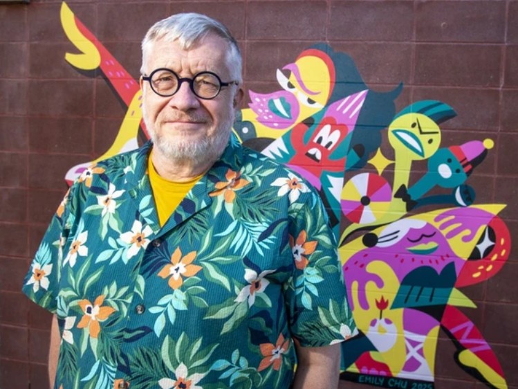 Gerald Osborn stands in front of a colorful mural smiling at the camera