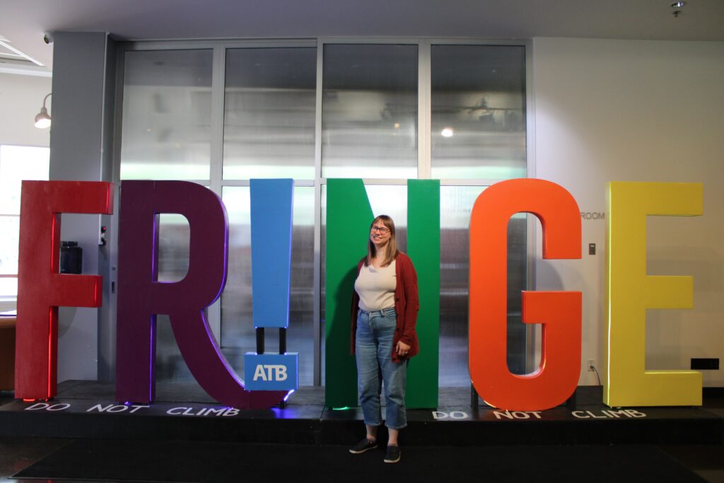A woman stands in front of a giant sign that spells out the word Fringe.