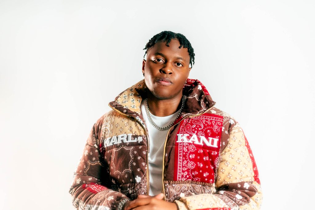 Artist is wearing a big puffer jacket and a gold chain necklace.