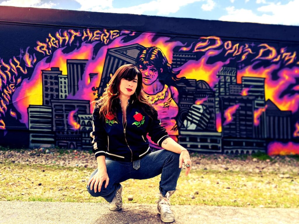 Artist poses in front of a mural.