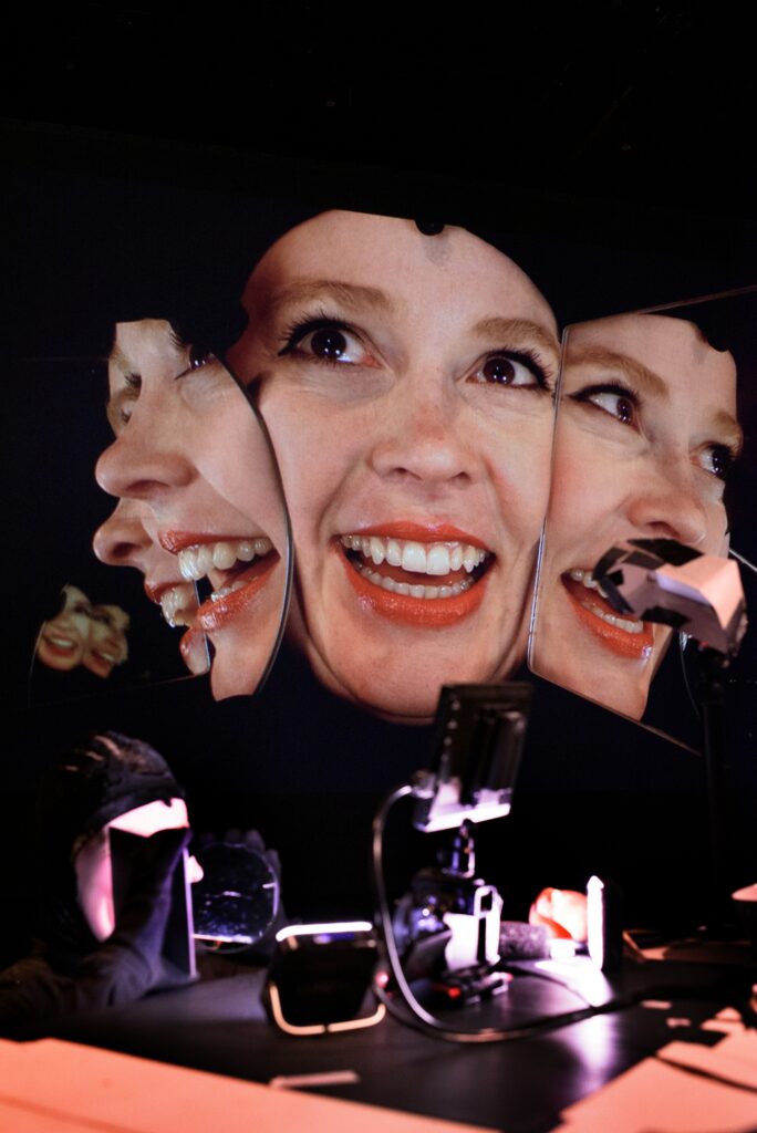 A Fringe Artist is kneeling in front of a mirror, reflecting four faces.