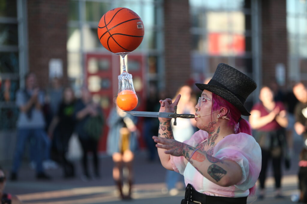 A street performer balances several objects on a knife held in her mouth.