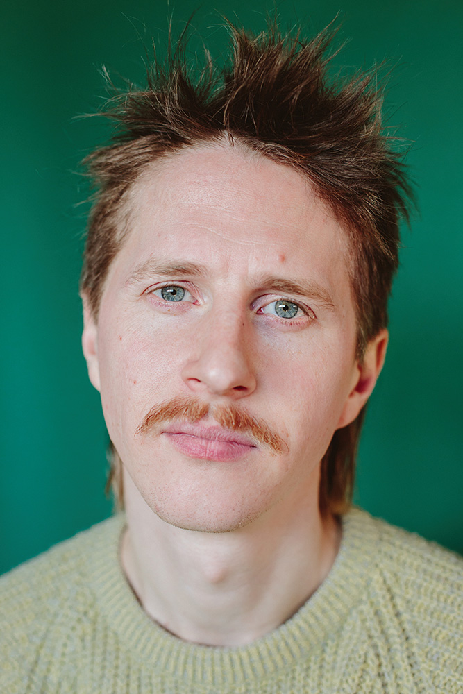 A headshot of Geoffrey Simon Brown with a green background.