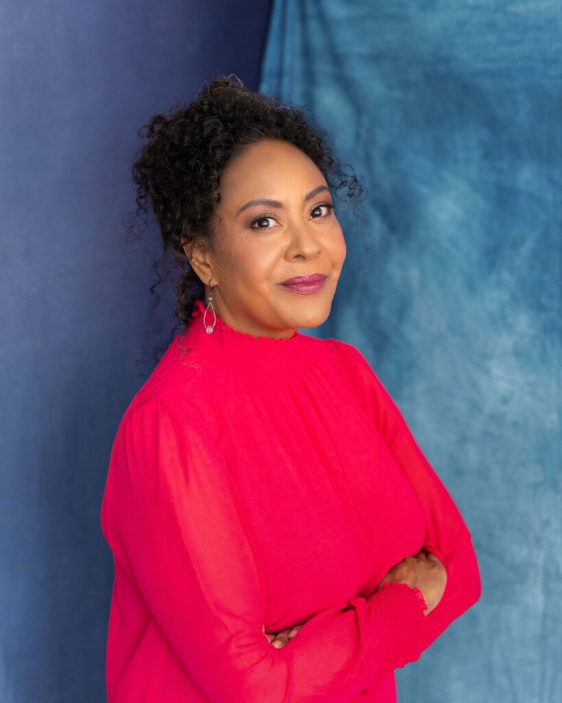 A headshot of Michelle Todd wearing a red top in front of a blue background.