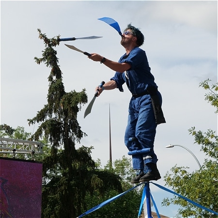 A performer balances on a pole while juggling.